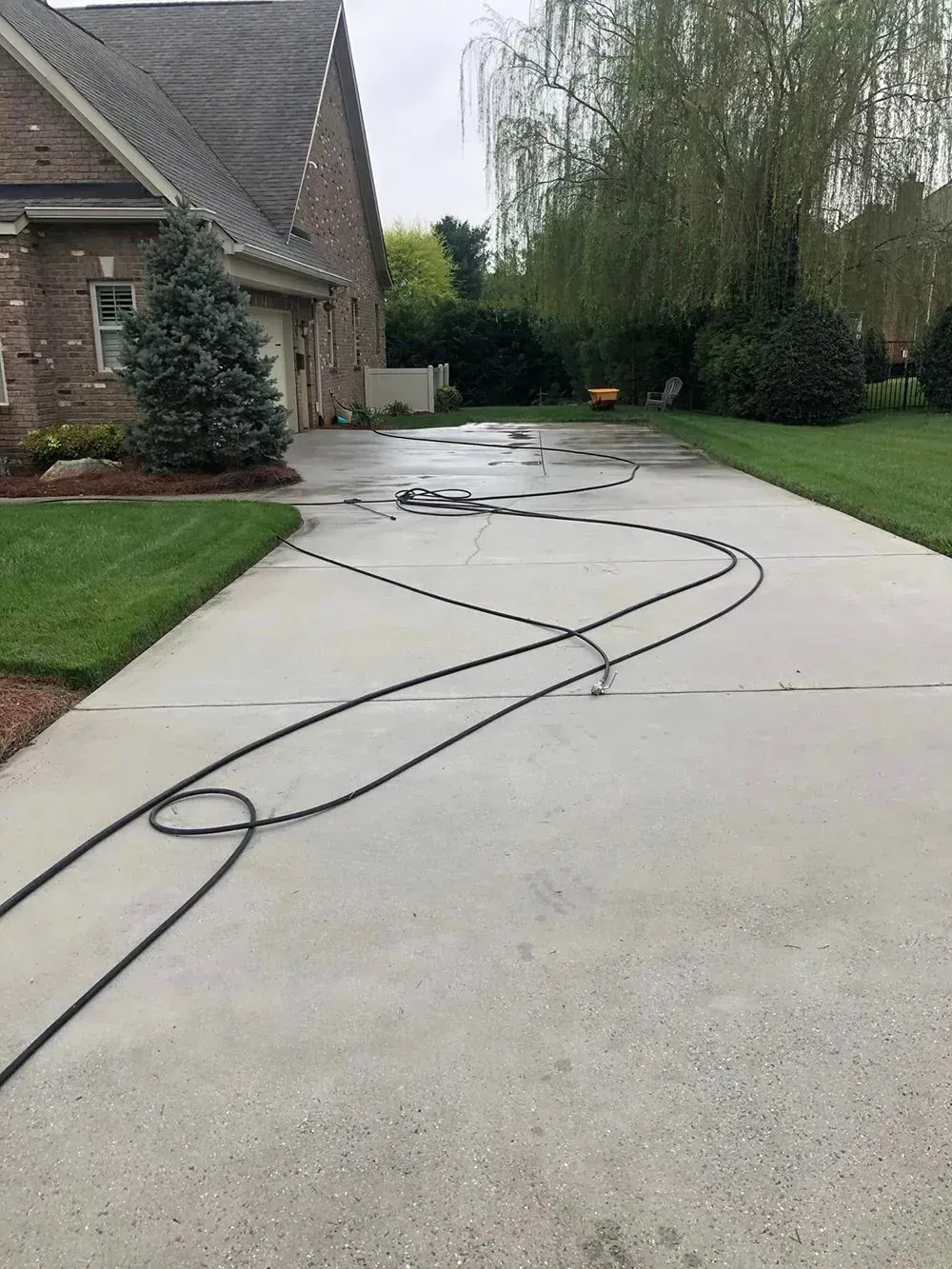A brick house with a driveway featuring long, coiled black hoses spread across the concrete surface.