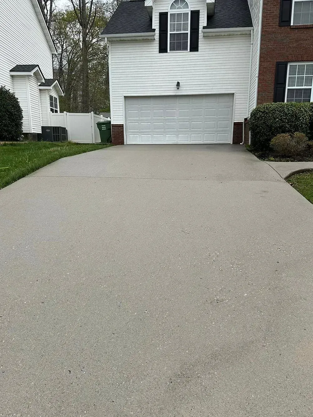 A paved driveway leading to a two-story home with white siding, a white garage door, and a brick section on the right.