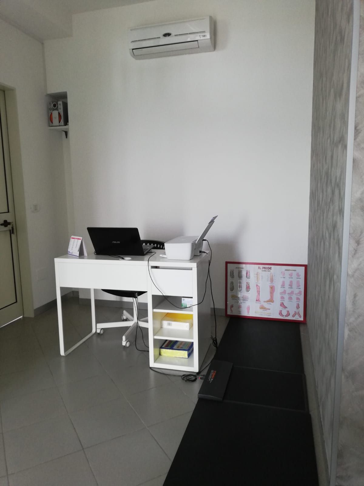 Una stanza con una scrivania, una sedia, un computer portatile e una stampante.