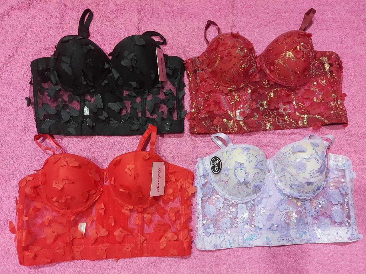 Cuatro sujetadores bustier coloridos: negro, rojo, rojo con motas doradas y lavanda/blanco.