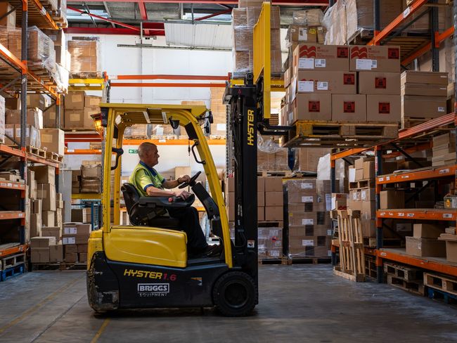 Man driving a yellow forklift in a warehouse, lifting a pallet of boxes.