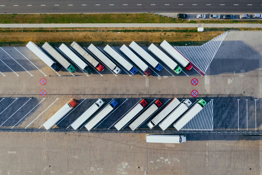 Overhead view of a truck stop with many semi-trucks parked, various colors, near road.