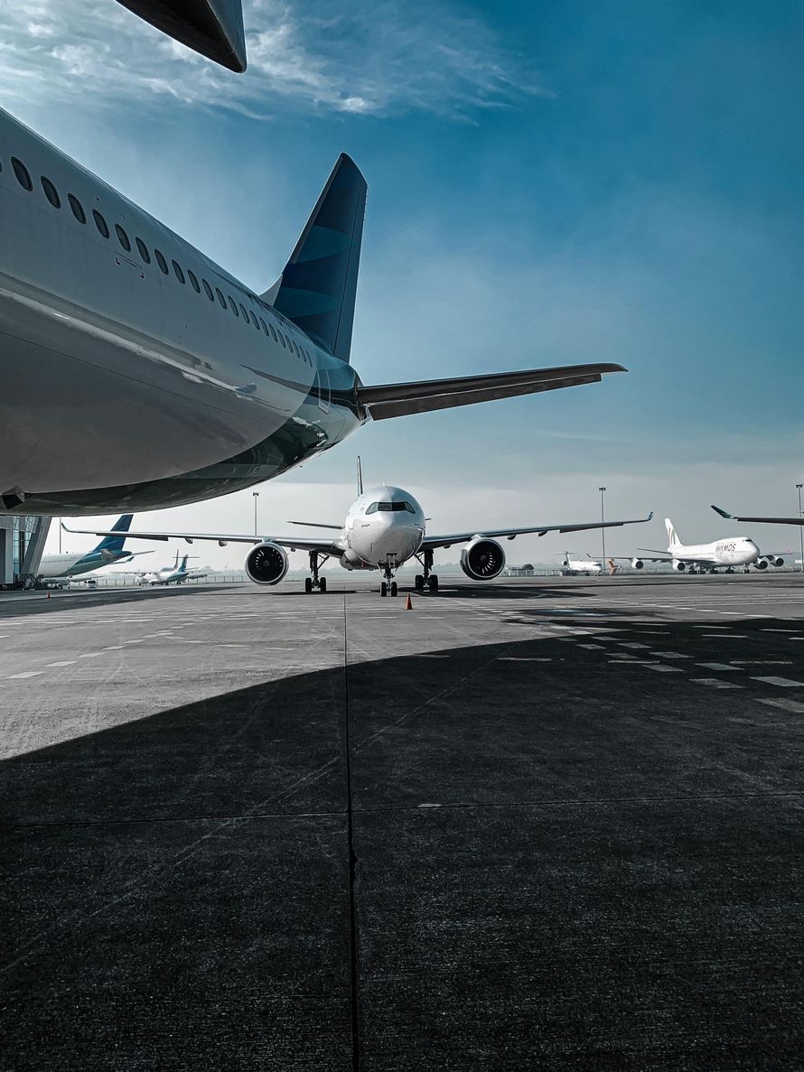 Airplane on tarmac, view from the side of another plane, blue sky. Other planes in the background.