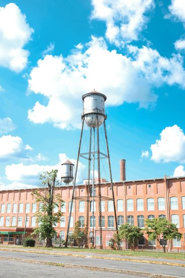 A water tower is in front of a large brick building.