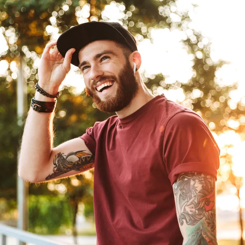 man with tattoos and beard wearing a ballcap and smiling