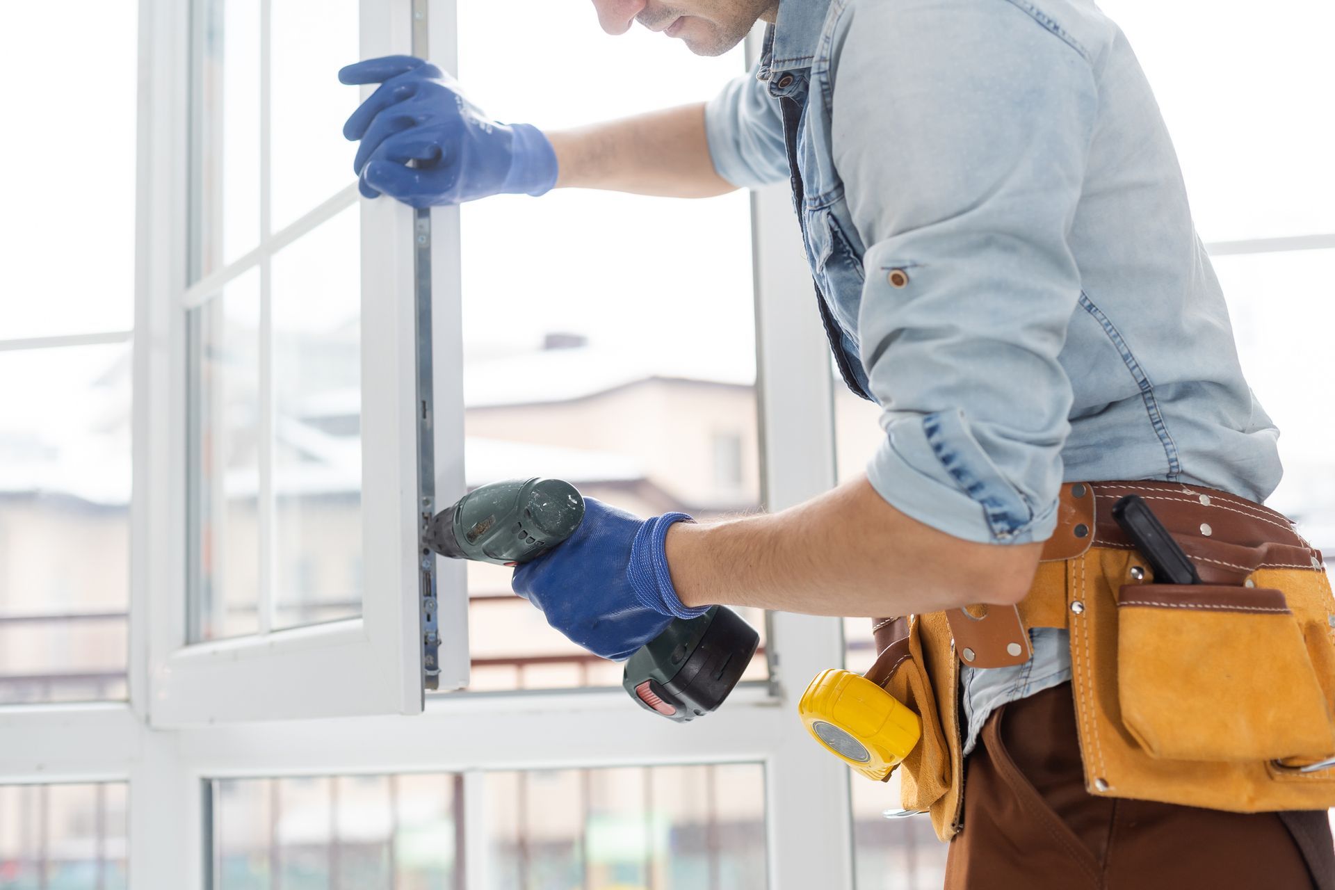 A worker wearing blue gloves and using a screwdriver, for glass window replacement at a home.