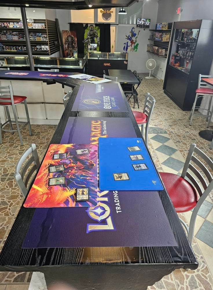 A game store with a table set for trading card games; cards are visible on mats.
