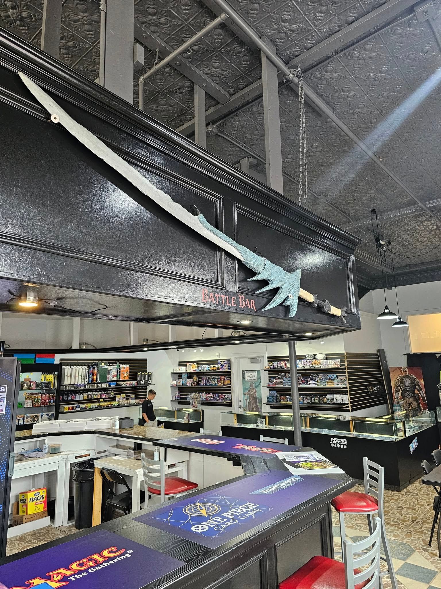 A large, pixelated sword displayed above a card game shop's counter; shop interior.