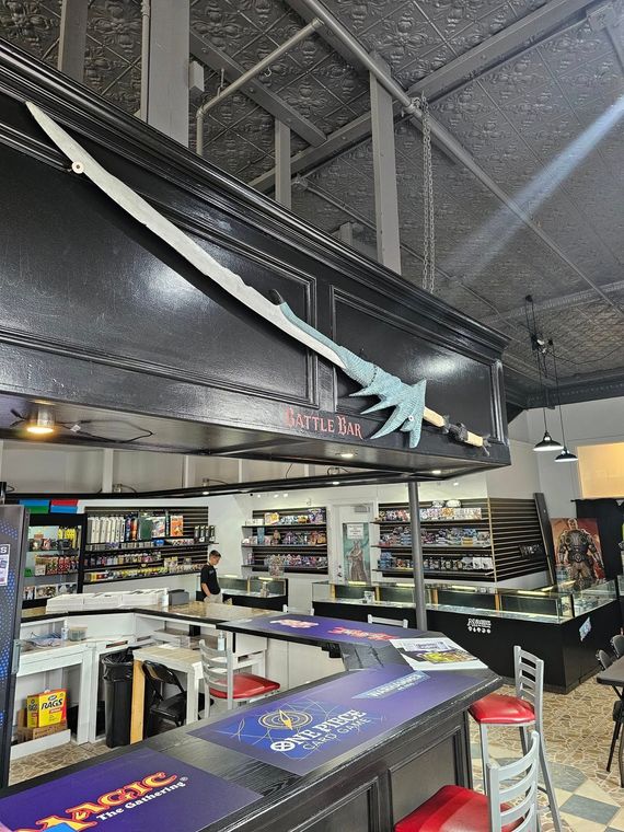 A sword decorates a store, with shelves of products and a bar in the foreground.