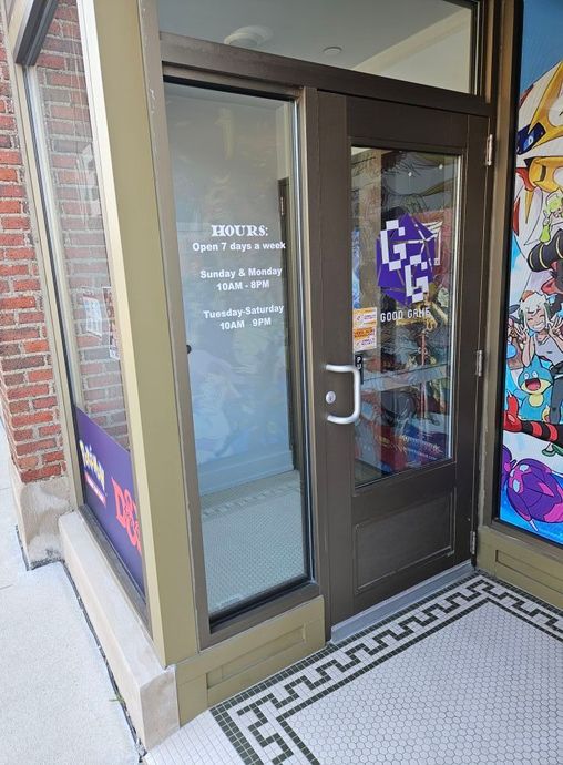 Exterior door to a store with opening hours. Brown doorframe, brick, glass, and tile.
