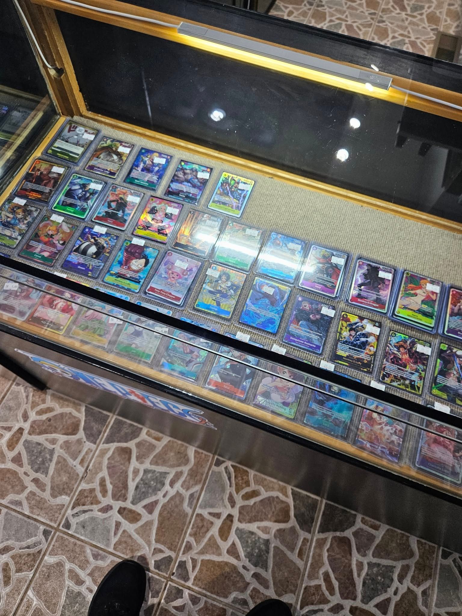 Display case of trading cards in a store, with rows of cards under glass, viewed from above.