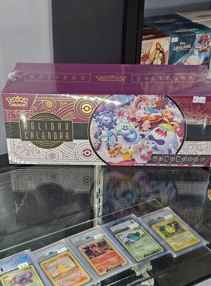 Sealed Pokémon Holiday Calendar box above graded cards. Display case, store setting.