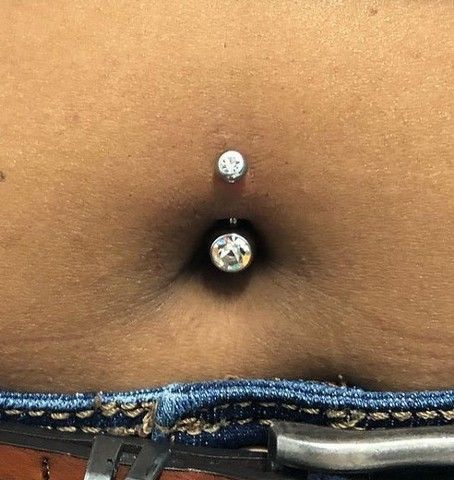 A close up of a person 's belly with a belly button piercing.