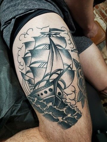 A man has a tattoo of a sailboat on his thigh.