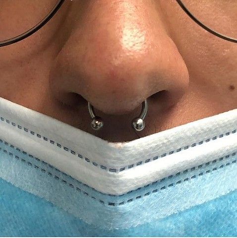 A close up of a person 's nose with a nose ring and glasses.