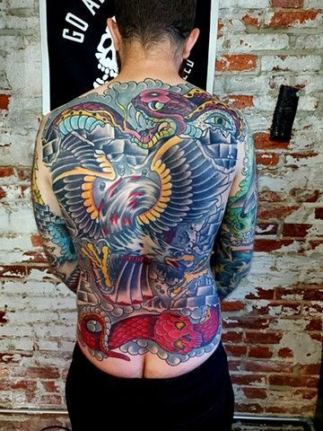 A man with a tattoo on his back is standing in front of a brick wall.