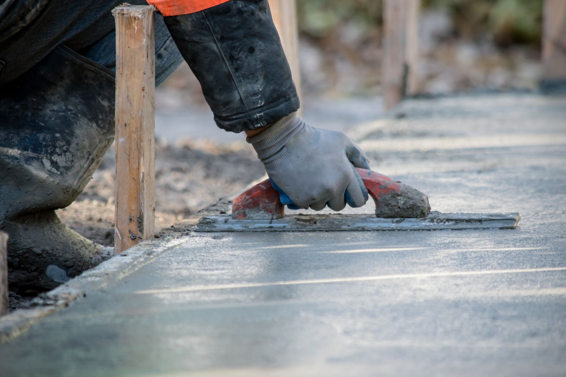 A man is using a trowel to spread concrete on a sidewalk.