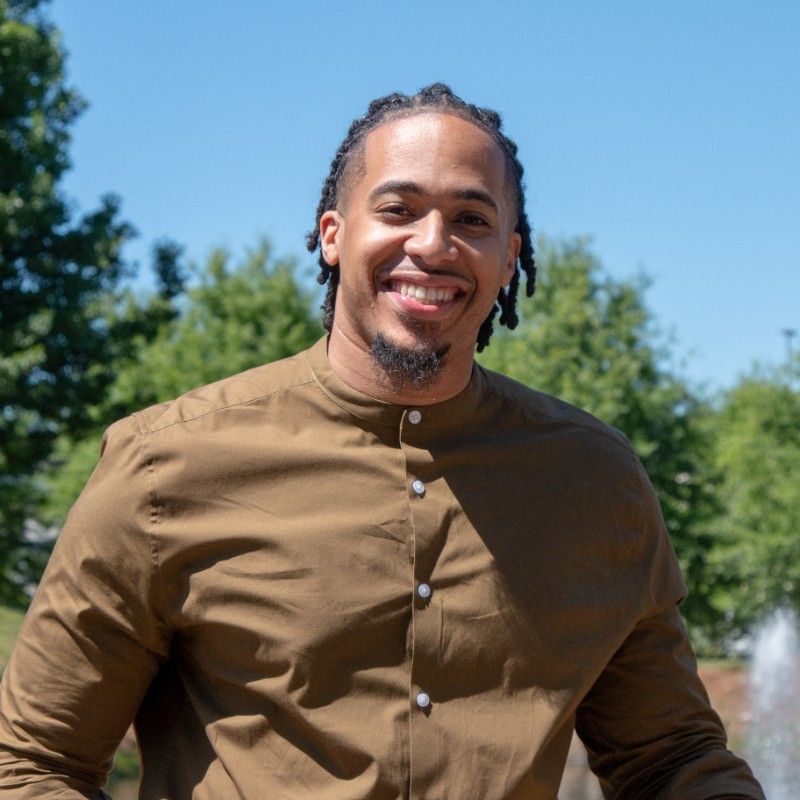 a man in a brown shirt is smiling in front of a fountain
