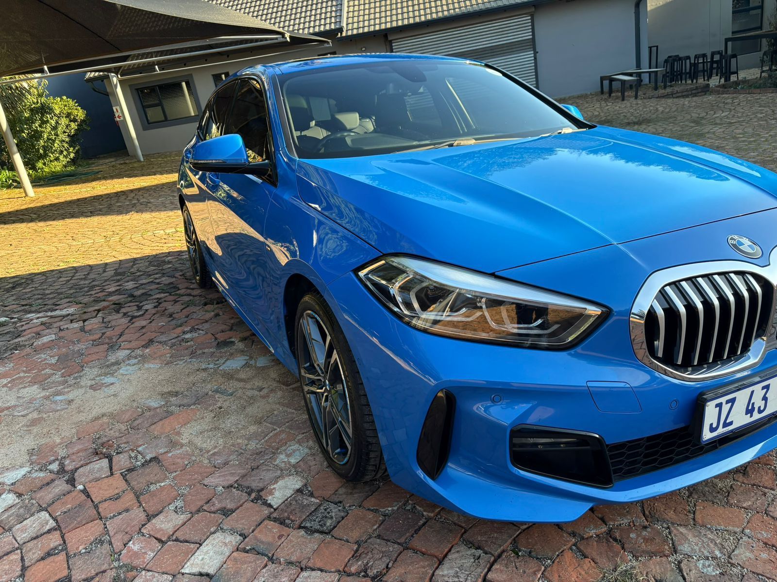 Blue BMW 1 series parked on a brick driveway.