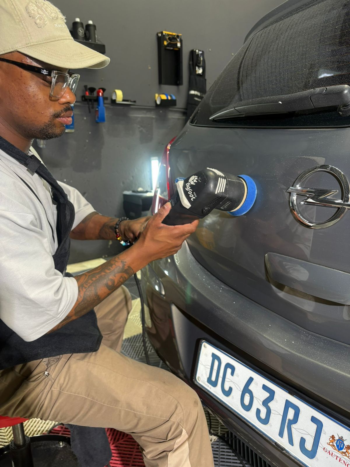 Man polishing a gray car with a machine in a workshop.
