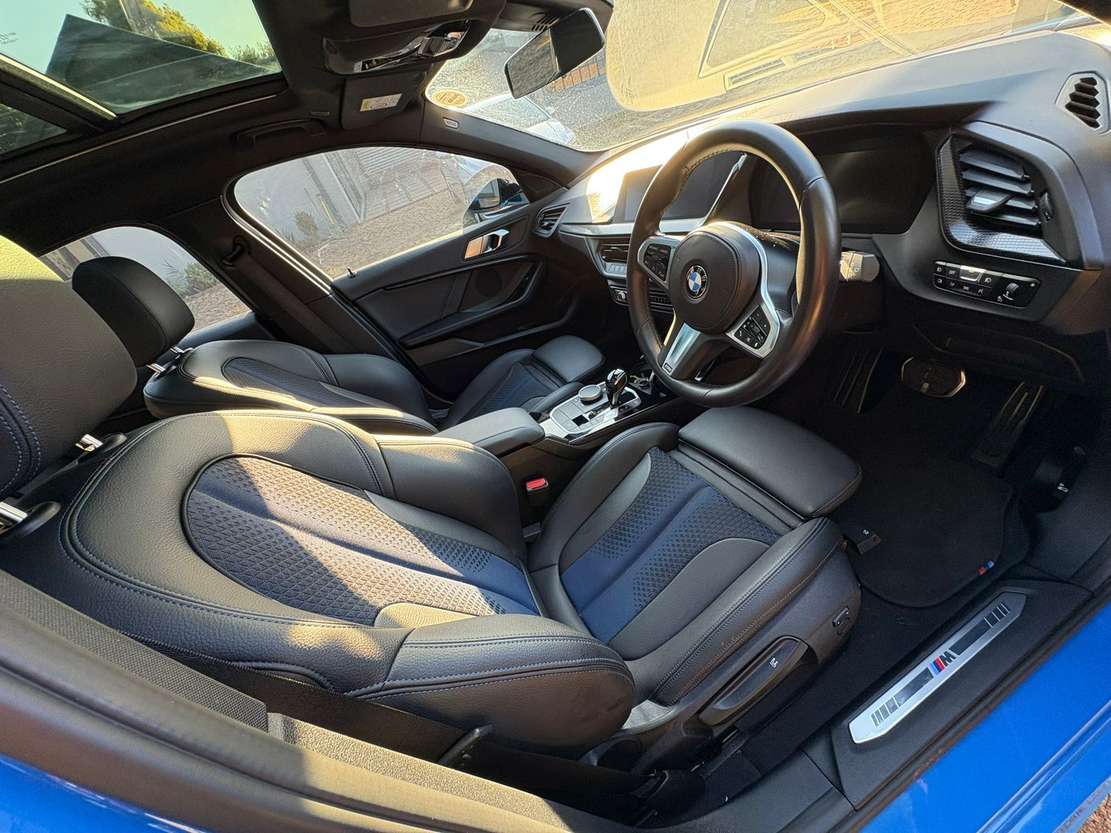 Interior view of a blue BMW, black leather seats, sunroof open, steering wheel visible.