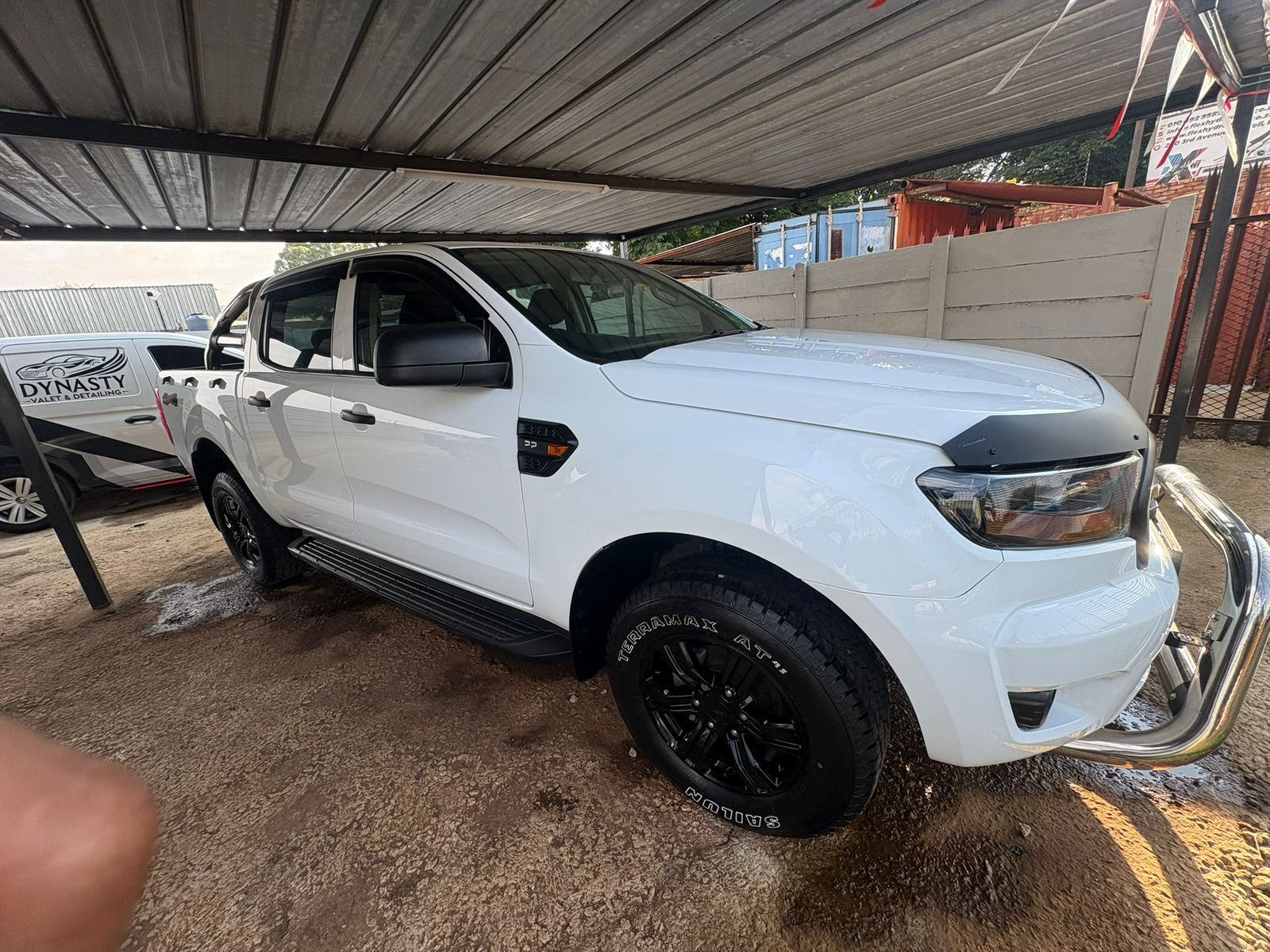 White Ford Ranger pickup truck with black wheels and bull bar parked under a carport.