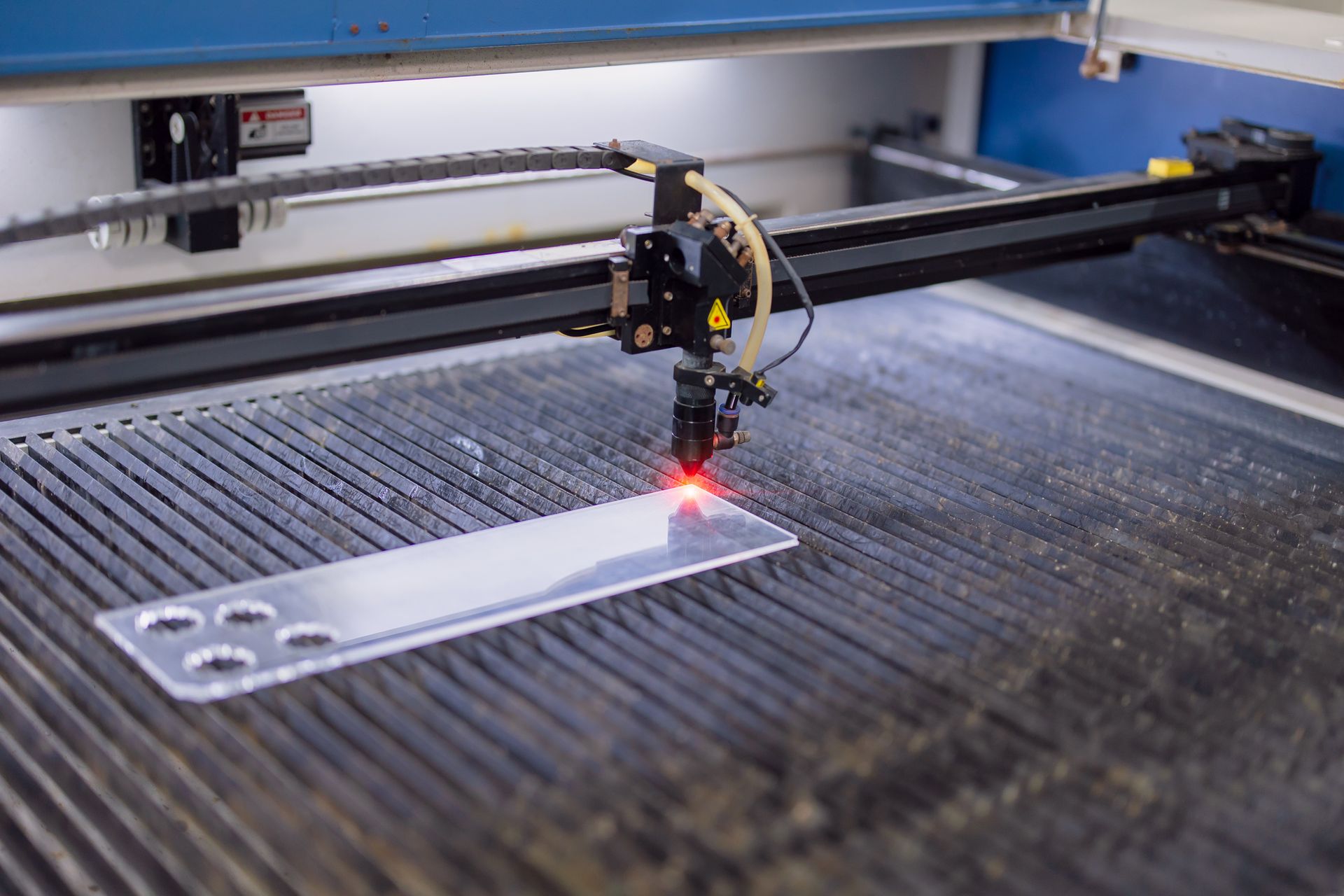 Laser cutting machine with a red laser cutting an acrylic piece on a grid-patterned surface.