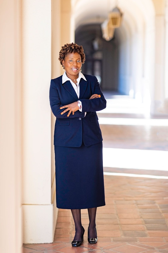 Woman in a navy suit stands with arms crossed in an arched hallway.