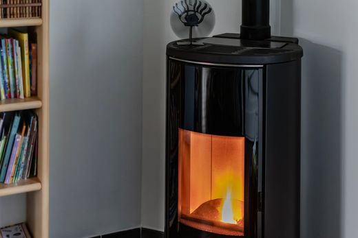 Stufa nera con fiamme arancioni, in un angolo di una stanza, accanto a una libreria con libri colorati.