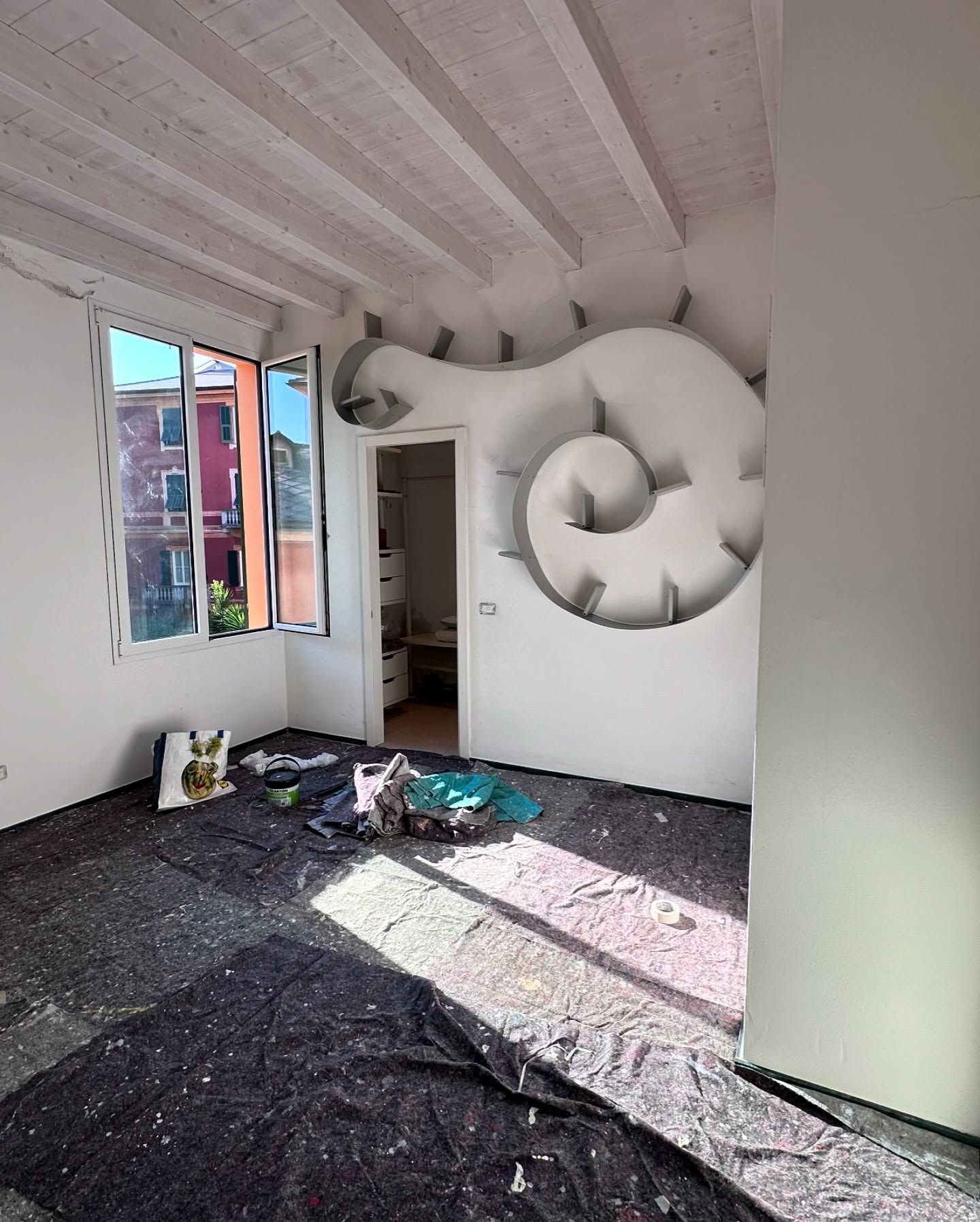Una stanza non finita con una parete bianca su cui spicca un grande murale a spirale con effetto 3D e teli scuri sul pavimento.