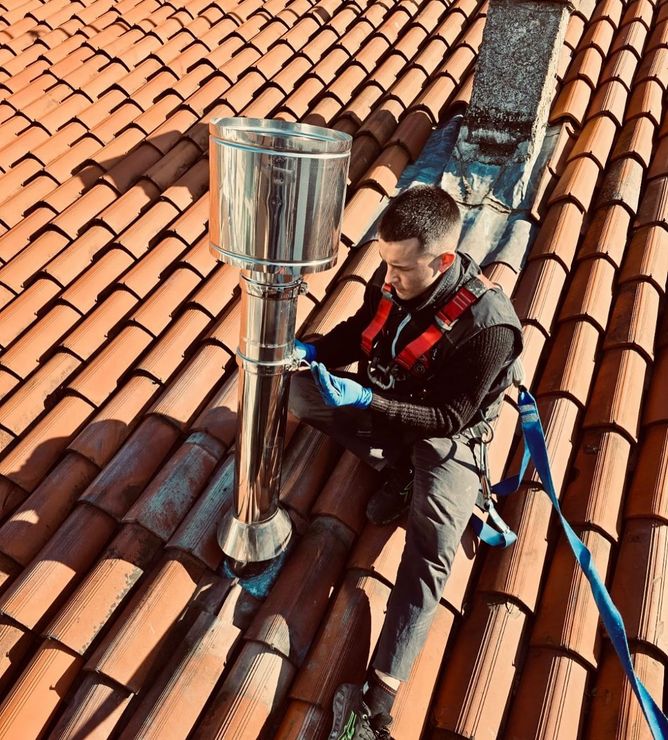 Uomo con imbracatura di sicurezza su un tetto di tegole, mentre installa un camino in acciaio inossidabile.