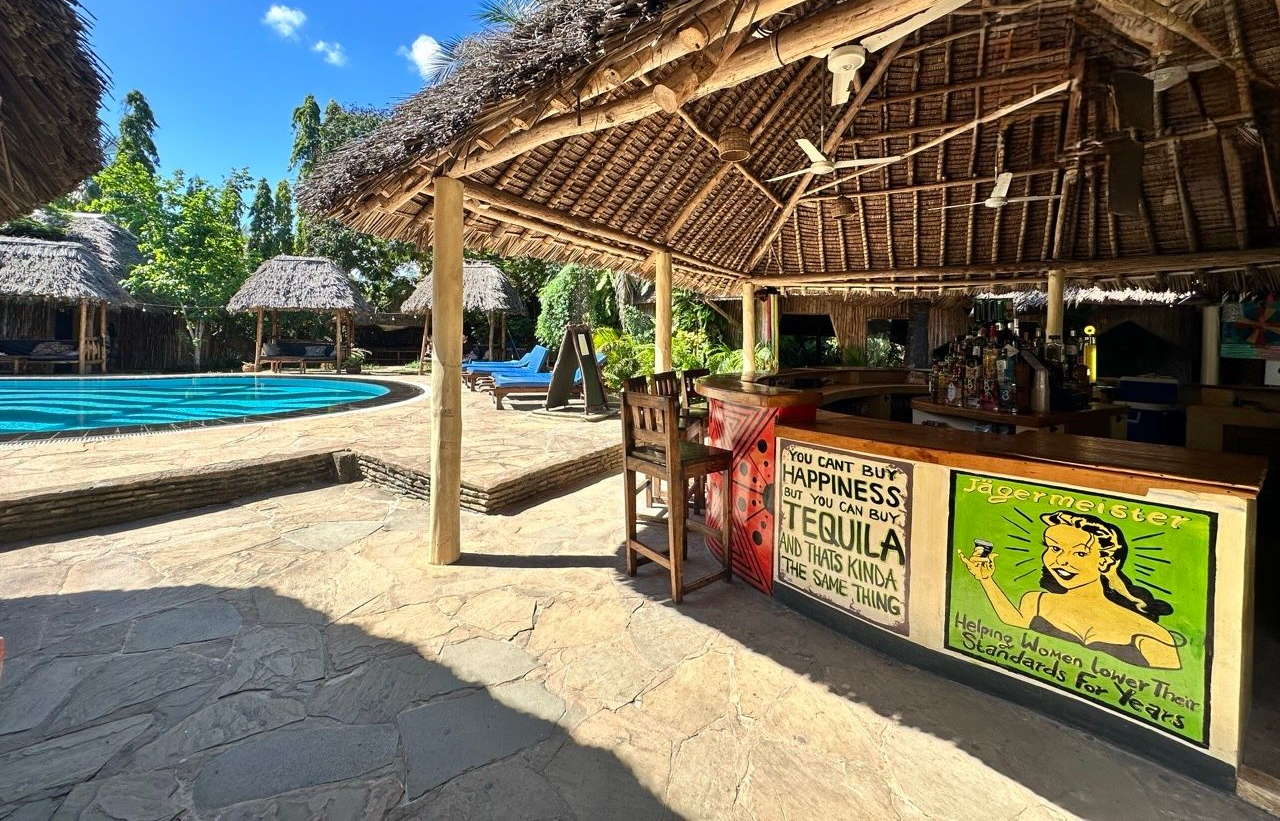 Beach scene: white sand, turquoise water, island in background, umbrella over two lounge chairs.
