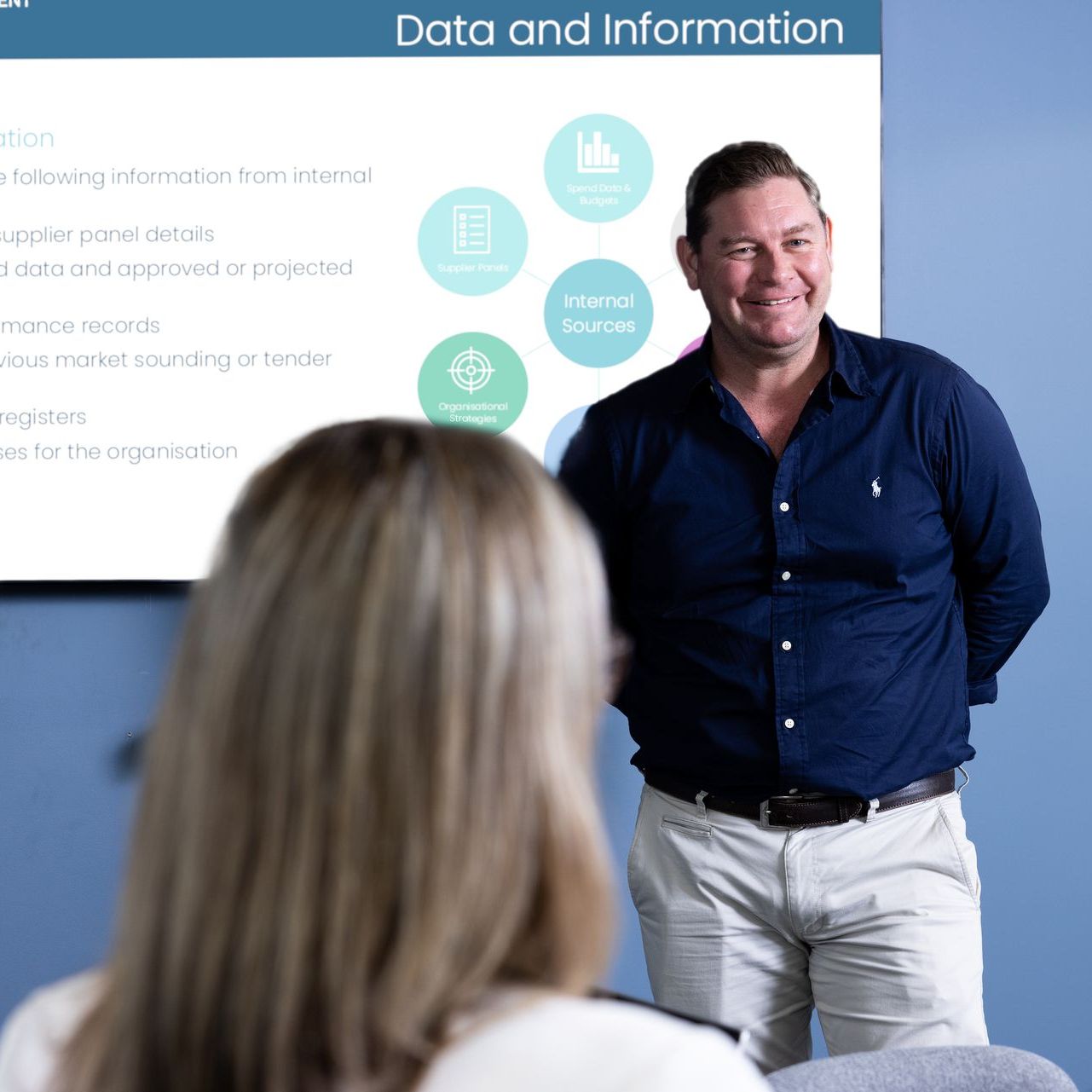 A man stands in front of a screen that says data and information