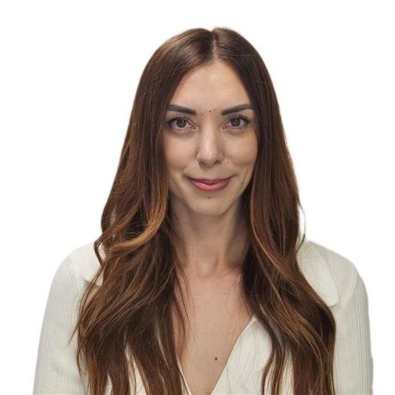 A woman with long brown hair is wearing a white jacket and smiling.
