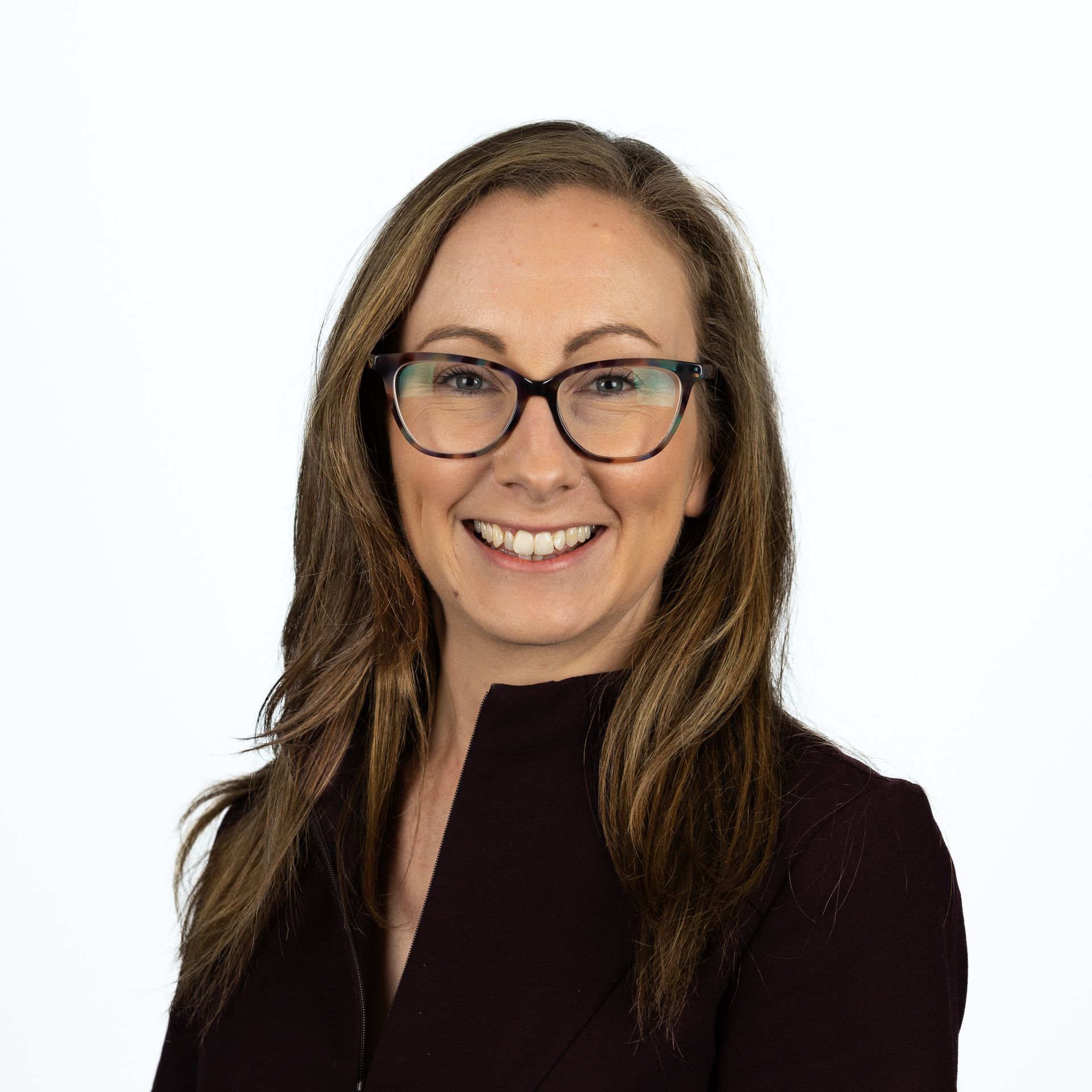 A woman wearing glasses and a black jacket is smiling for the camera.