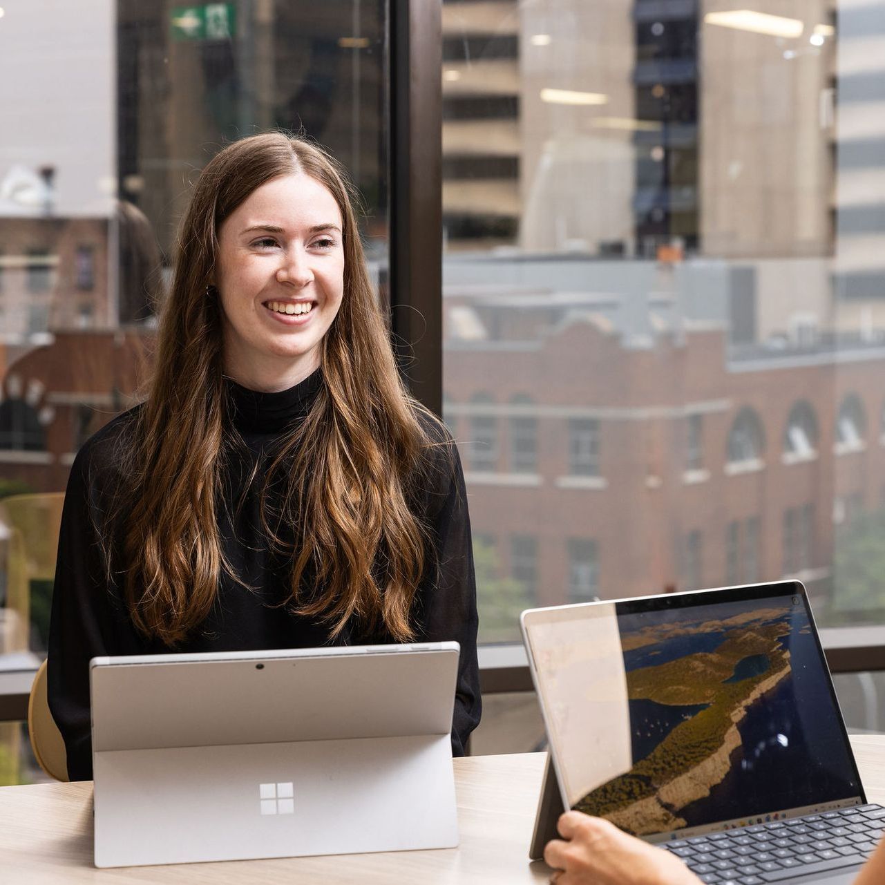 A woman is sitting at a table with a laptop and a tablet.