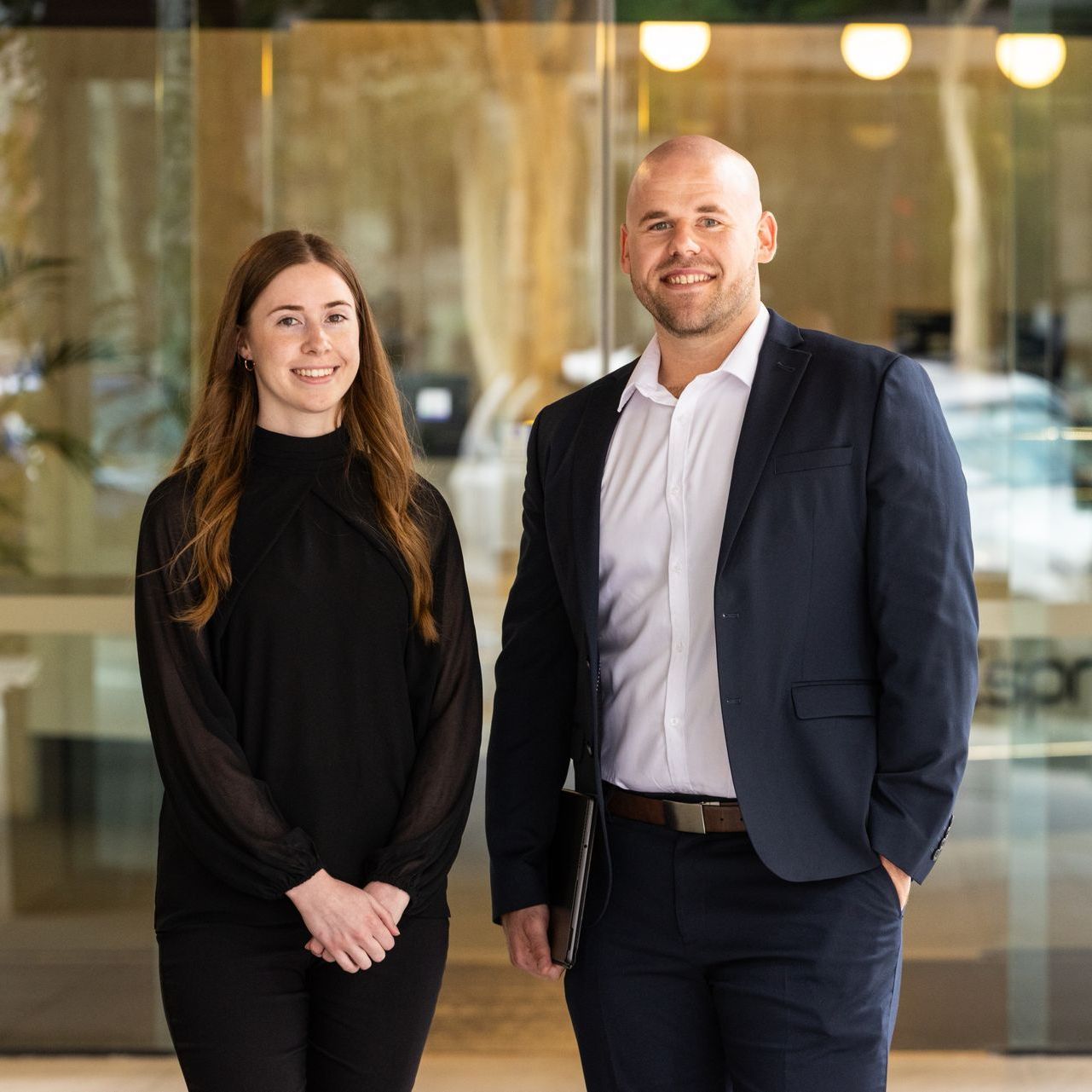 A man and a woman are standing next to each other in front of a glass wall.