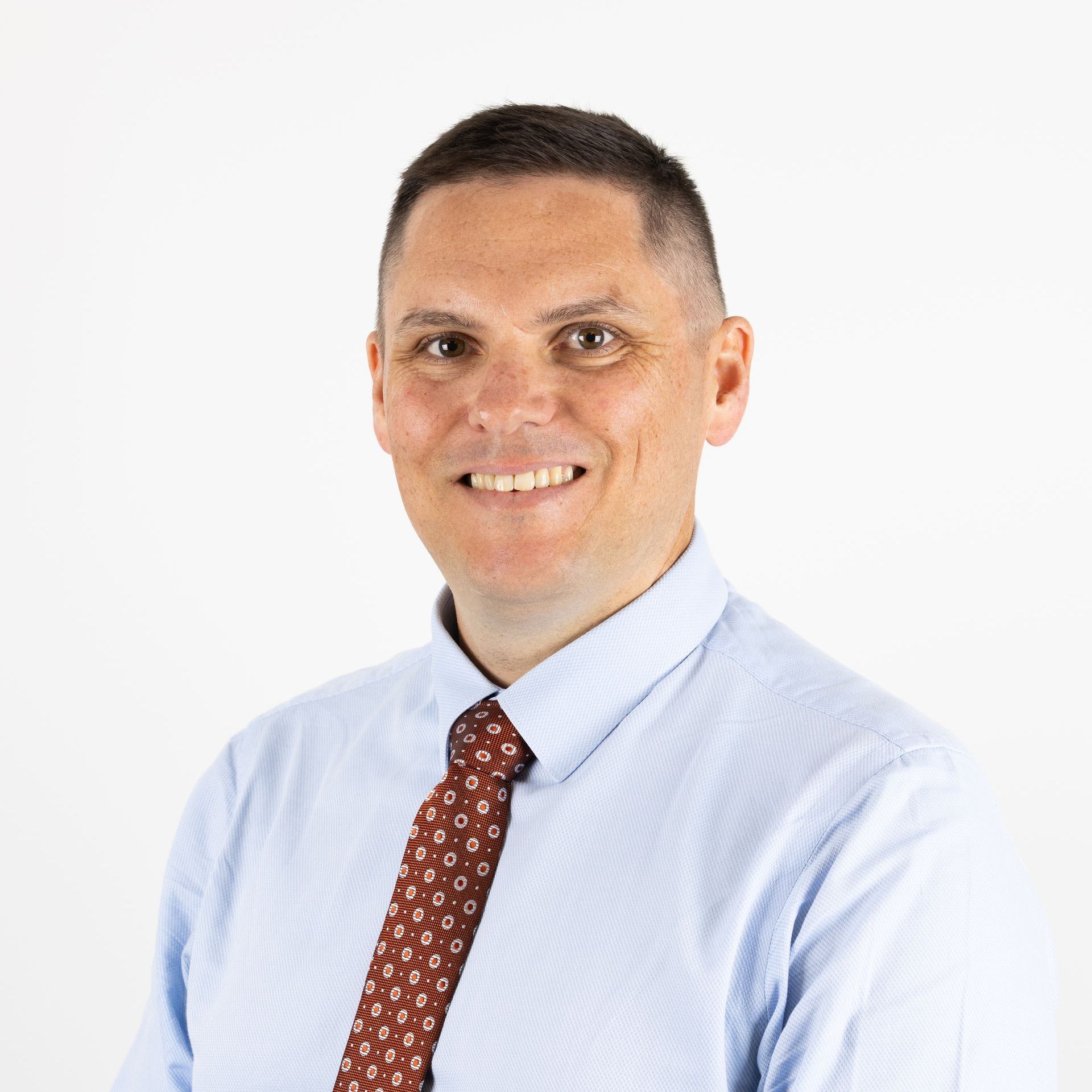A man in a blue shirt and tie is smiling for the camera.