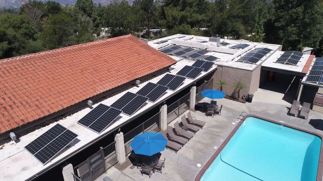 Solar panels on a roof next to a pool with lounge chairs and umbrellas.