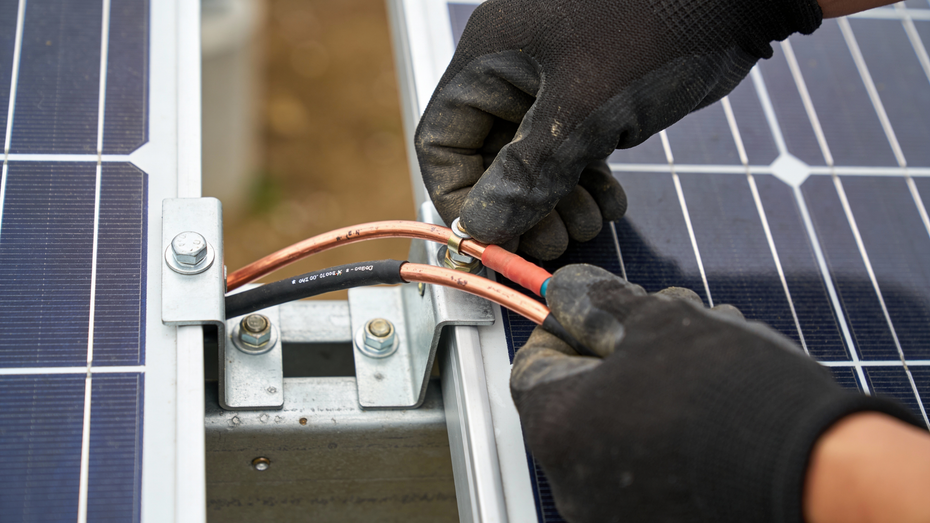 Hands in black gloves connecting wires to a solar panel array.