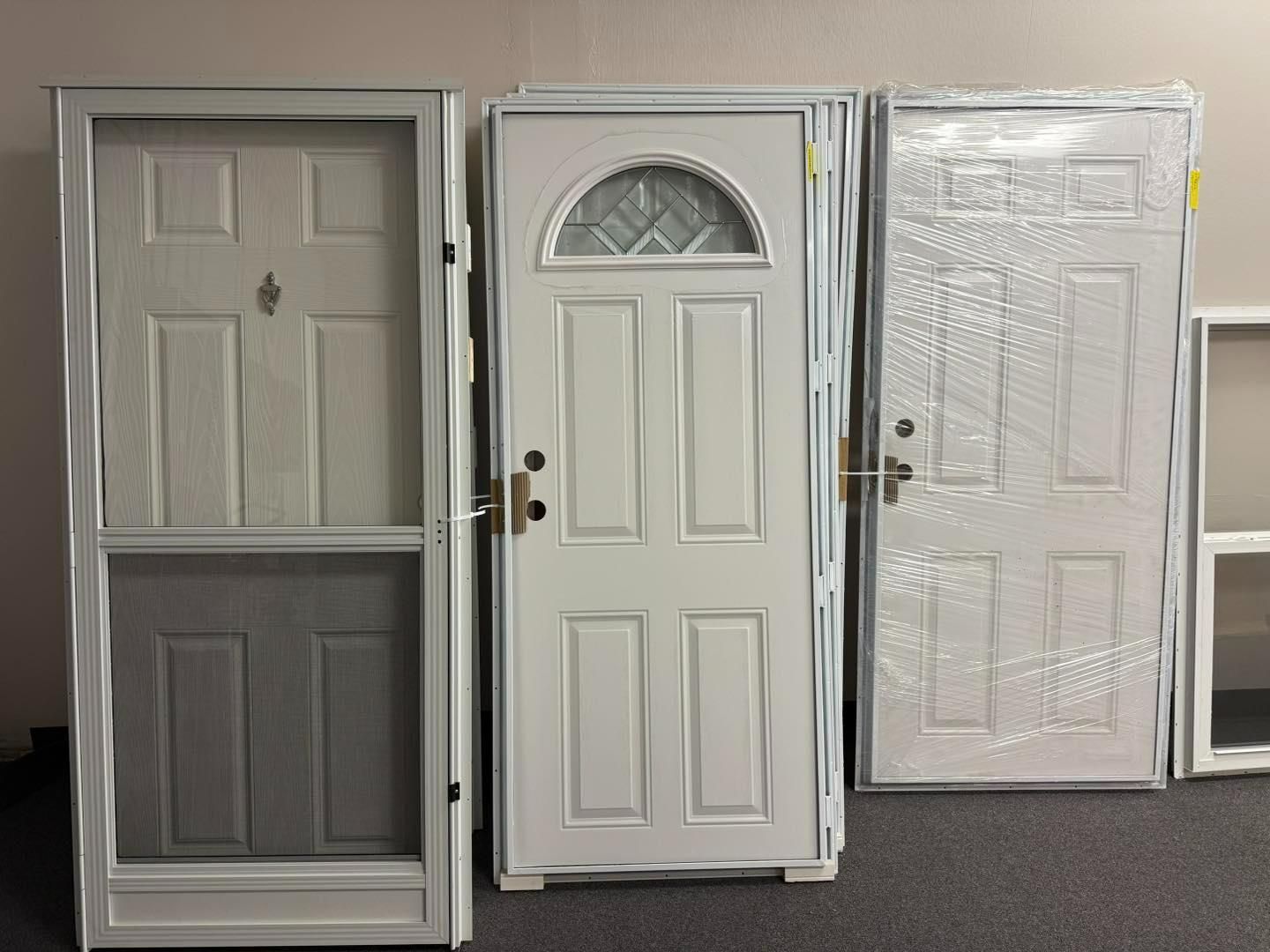 Three white exterior doors with different styles, on a dark carpet.