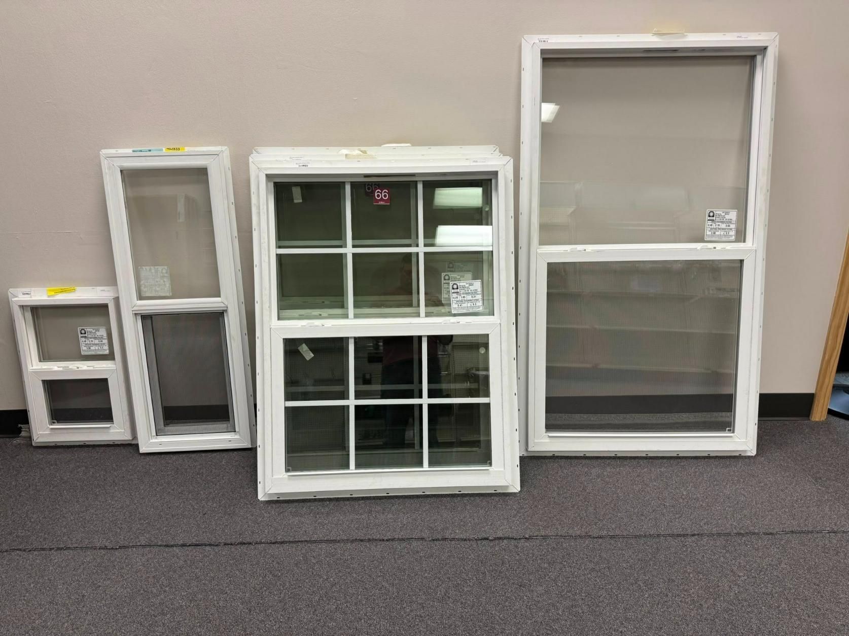 Five white-framed windows of varying sizes, displayed indoors on a carpeted surface, against a beige wall.