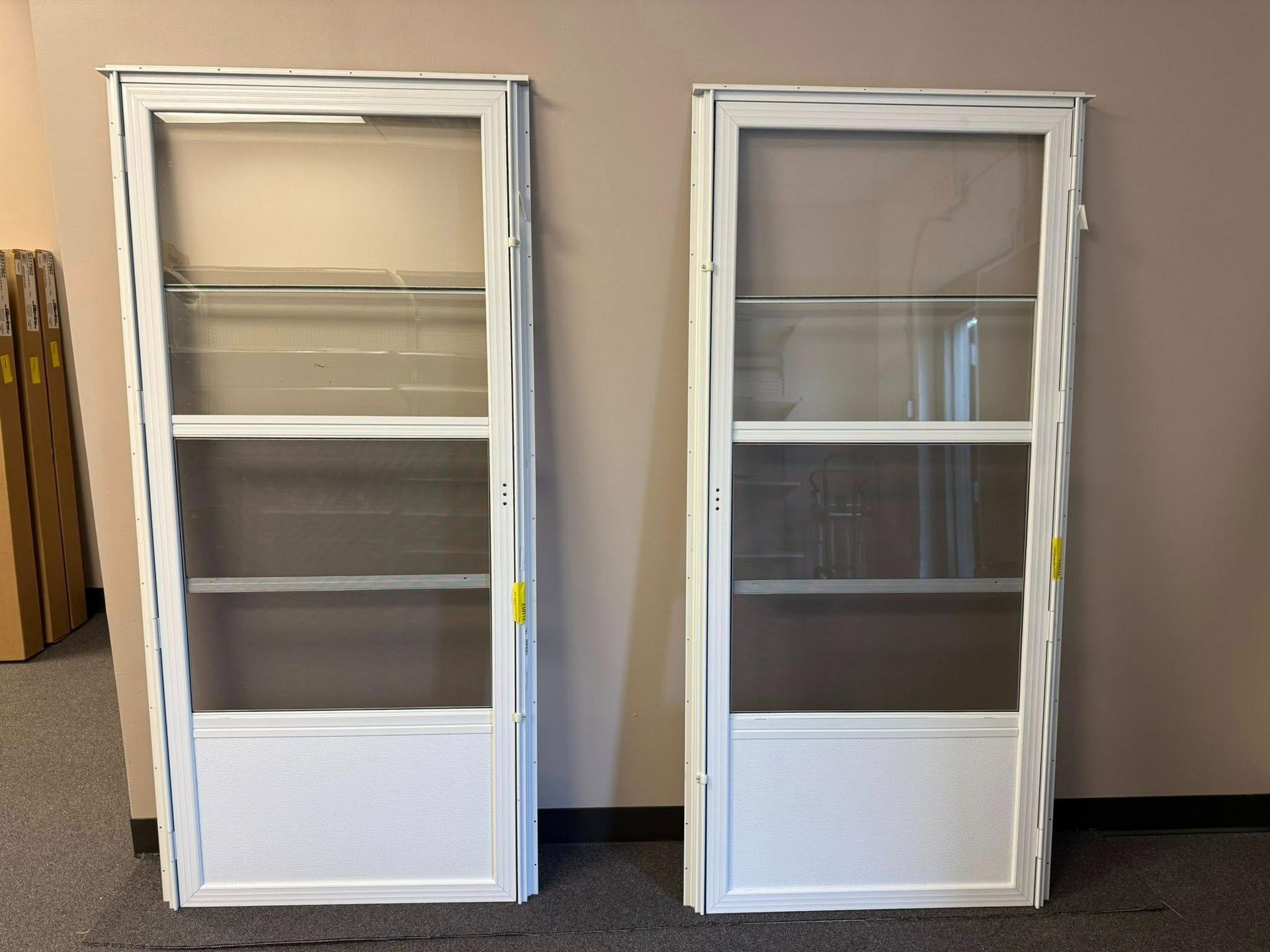 Two white screen doors, standing upright indoors, against a neutral wall.