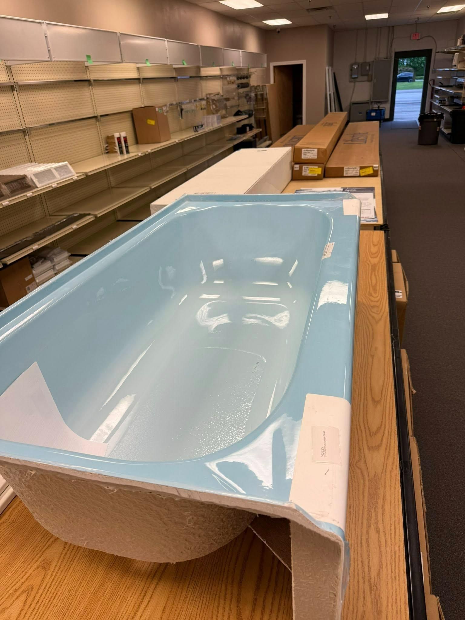 A light blue bathtub on a wooden table in a store with empty shelves.