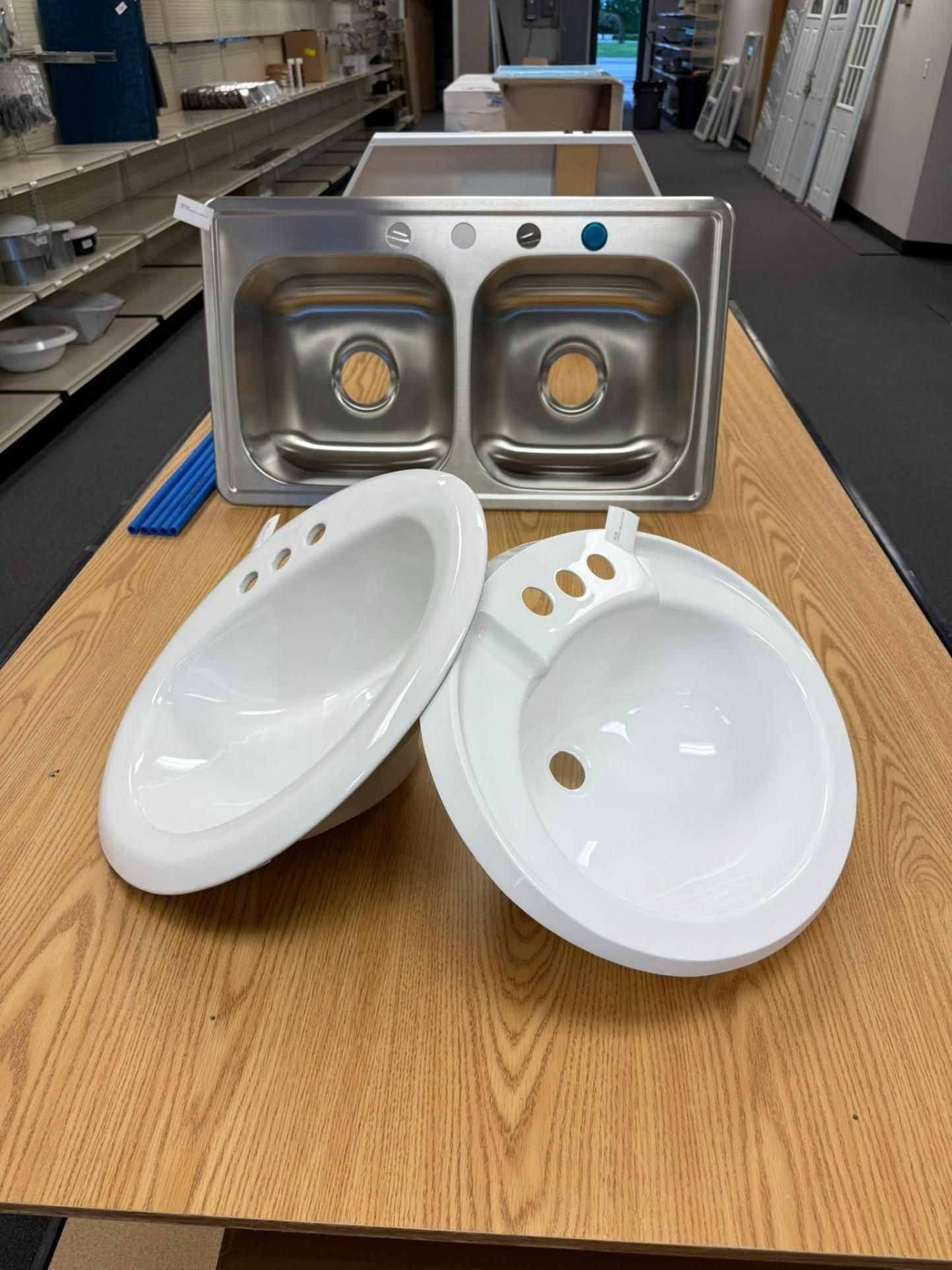 Two white sinks and a stainless steel double sink on a wooden table in a store.