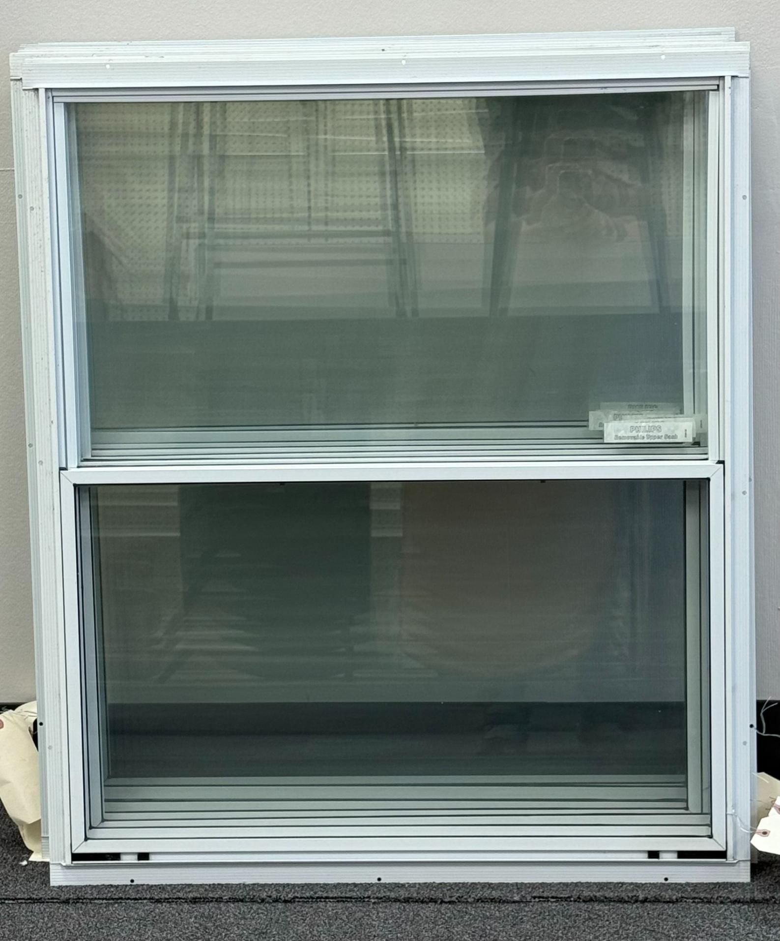 White double-hung window with a screen, indoors, against a light gray wall.