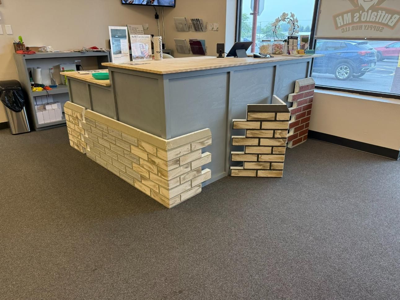 Counter with brick veneer samples in a store, grey floor, and a window with a car outside.