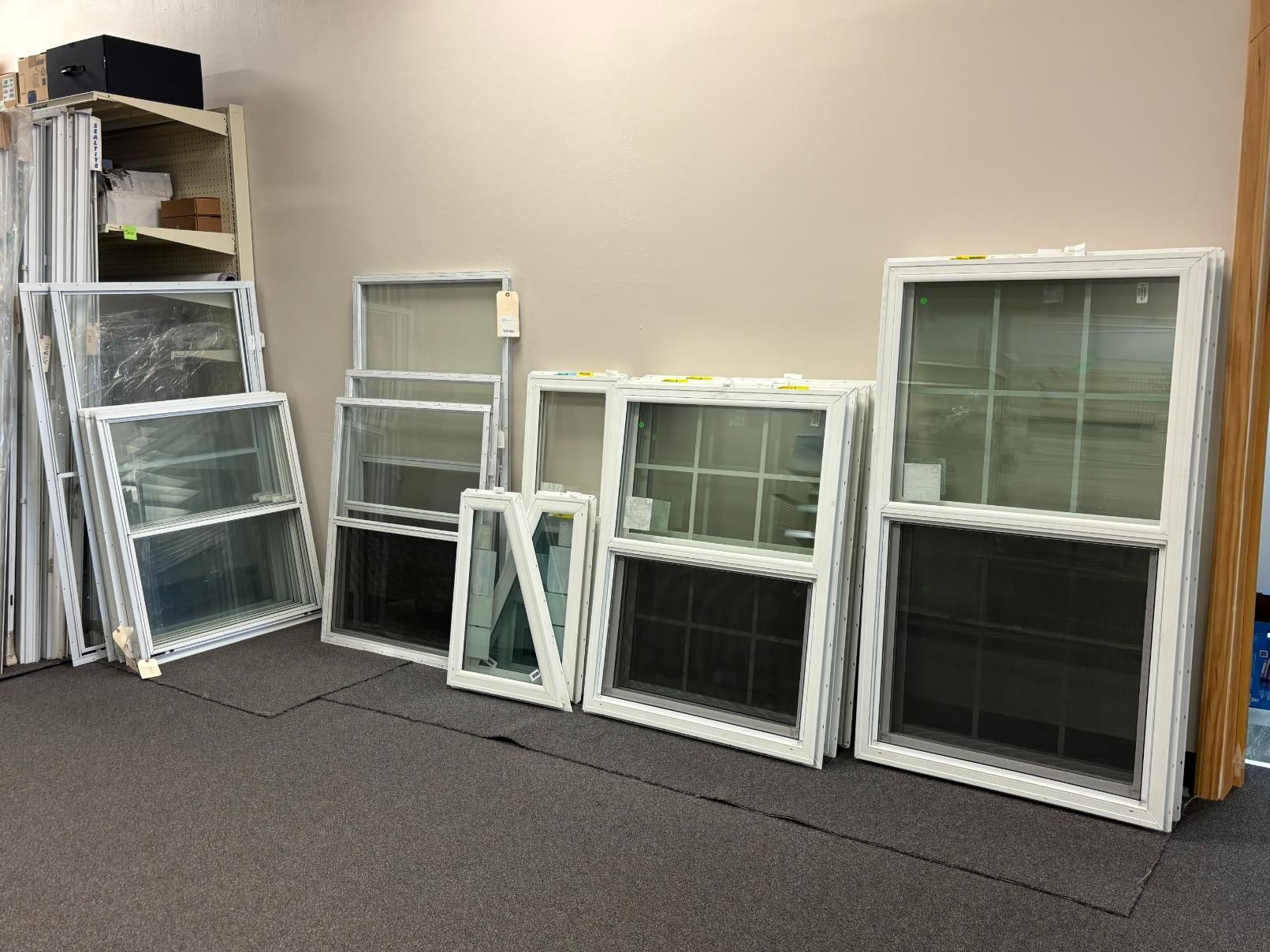 Assortment of white-framed windows of various sizes leaning against a wall in a room with a gray carpet.