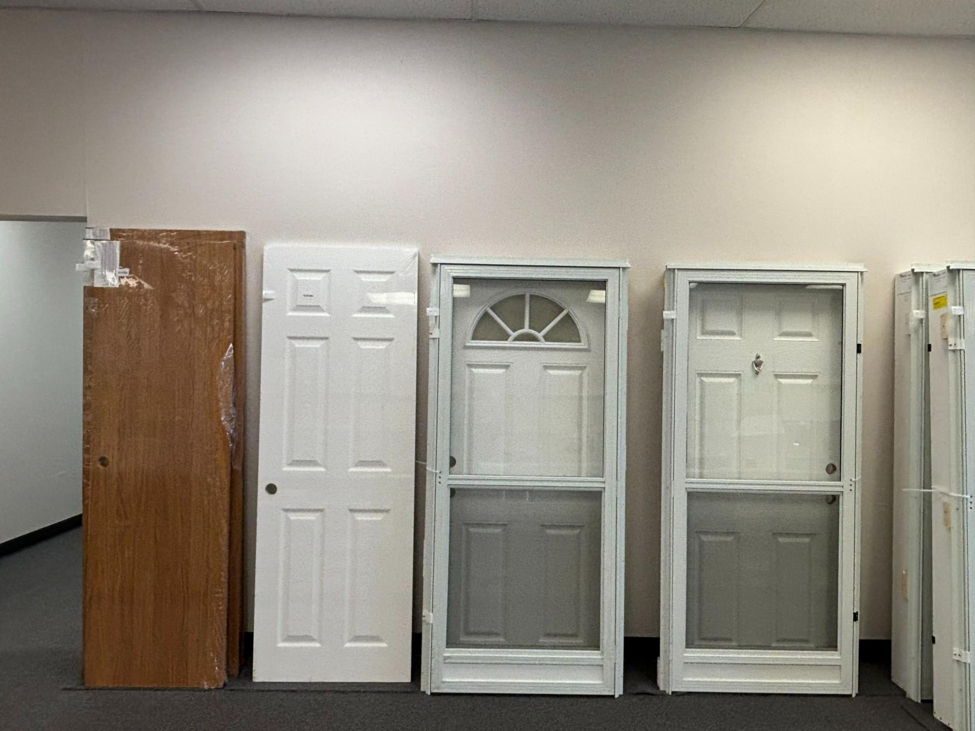 Doors of various types and colors leaning against a white wall in an indoor setting.
