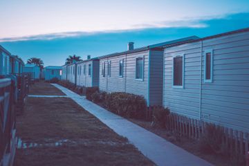 Row of white mobile homes with a pathway between them, under a blue dusk sky.